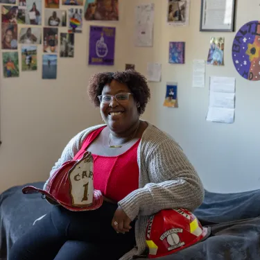 Diamond Jones in her Comstock room holding an antique fire helmet and smiling with photos behind her