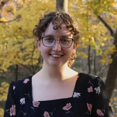 A profile photo of Claire Sullivan, smiling, in a flowered top, outside