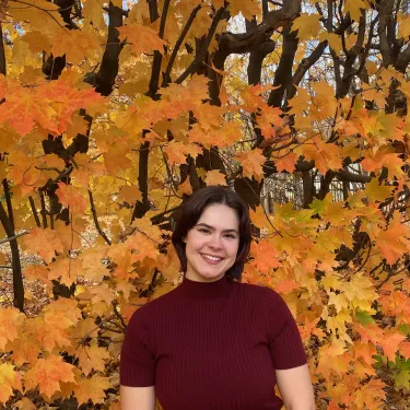 Katherine Booth, smiling, in front of bright orange fall folliage