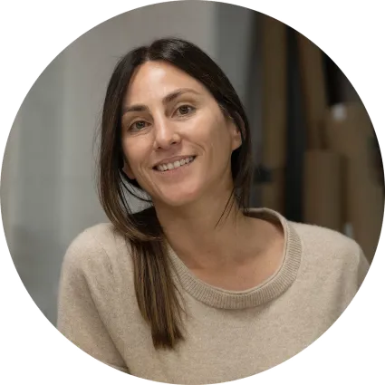 Portrait of a smiling woman with long brown hair parted down the middle and a beige knit sweater, set against an indoor background.