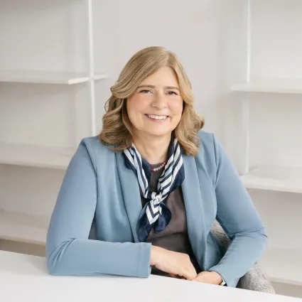 Portrait of Eva Rueschmann sitting at a white desk in a light-colored office with empty white shelves behind her.