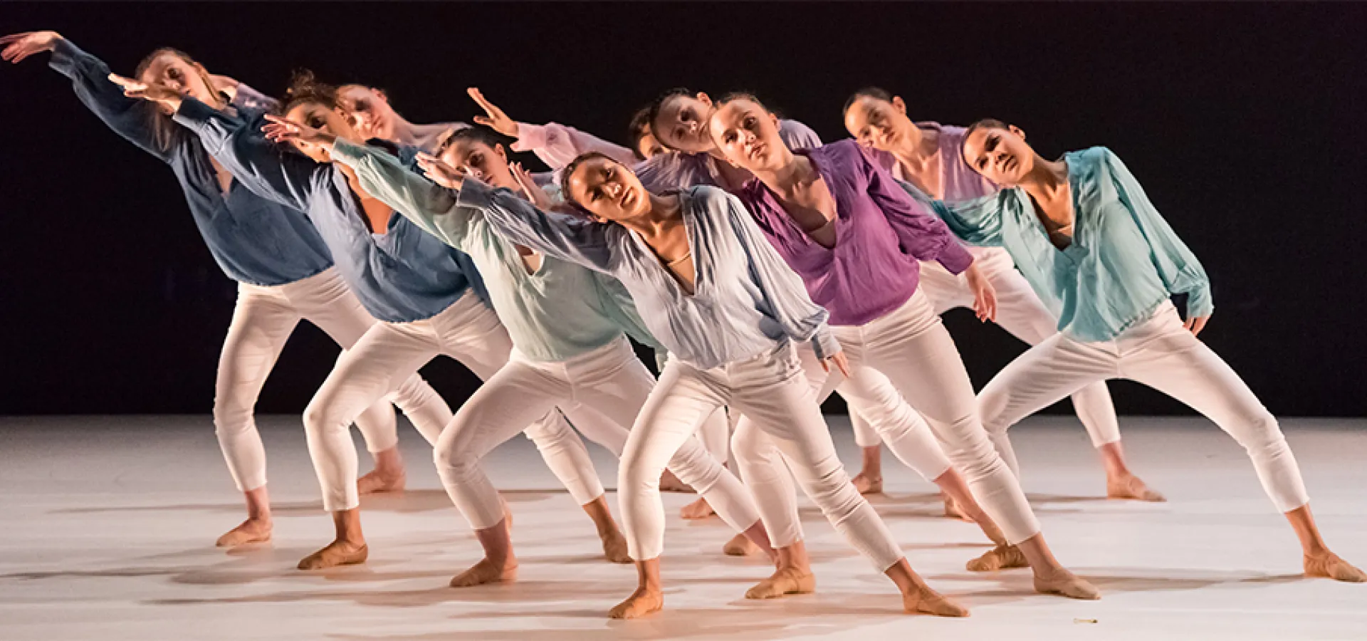 Group of dancers in white pants and differently colored tops