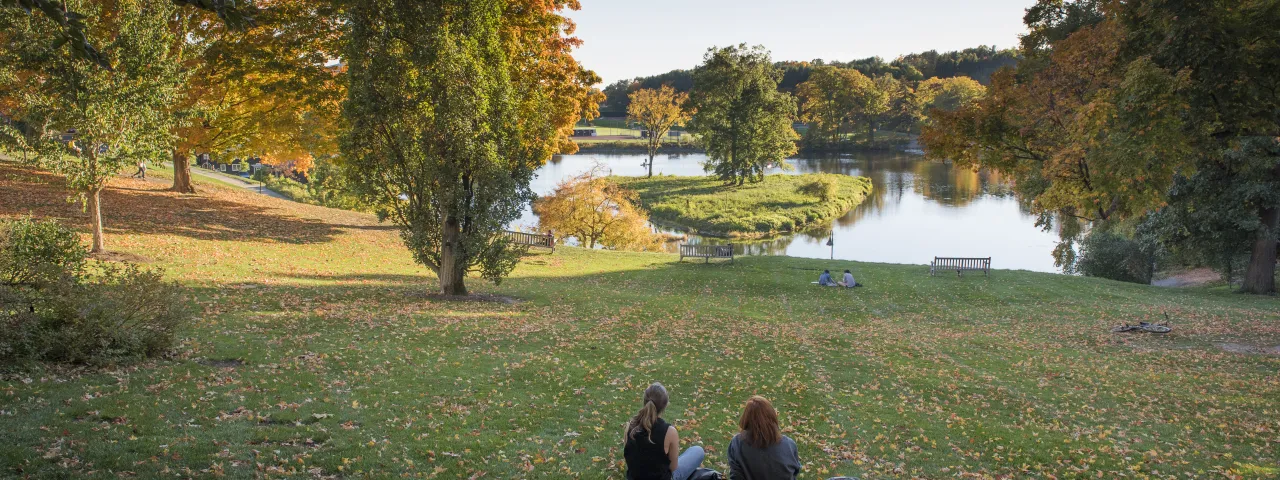 Two students sitting in front of Paradise Pond in the fall.