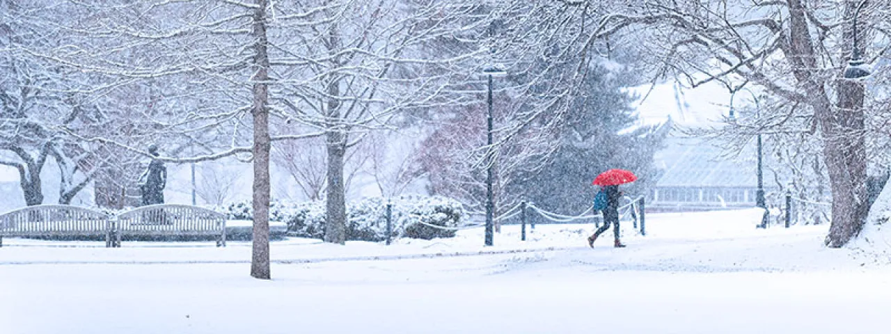 A single student with a red umbrella walking in a snowstorm