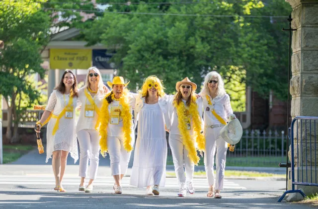 Several alums dressed in white arrive arm in arm on campus.