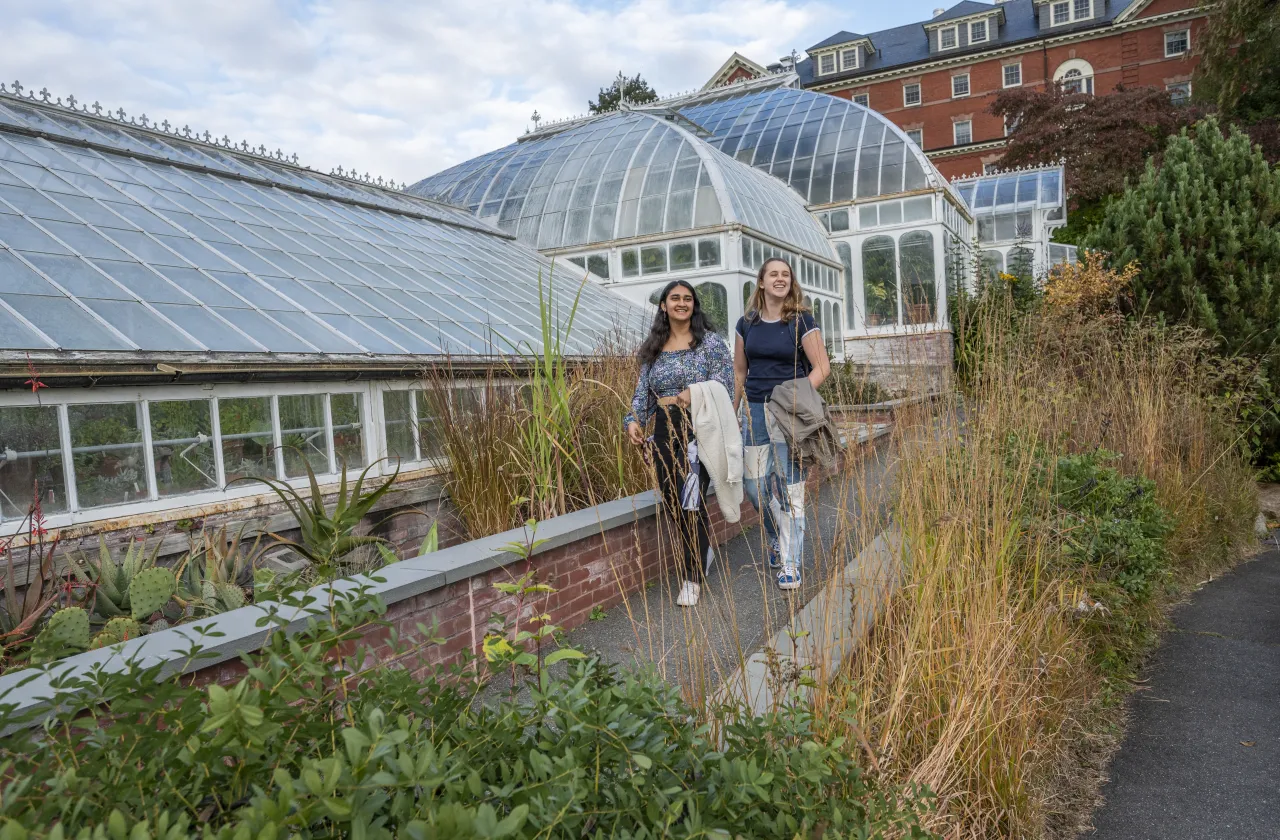 Two students walking in front of the Lyman Conservatory, smiling.