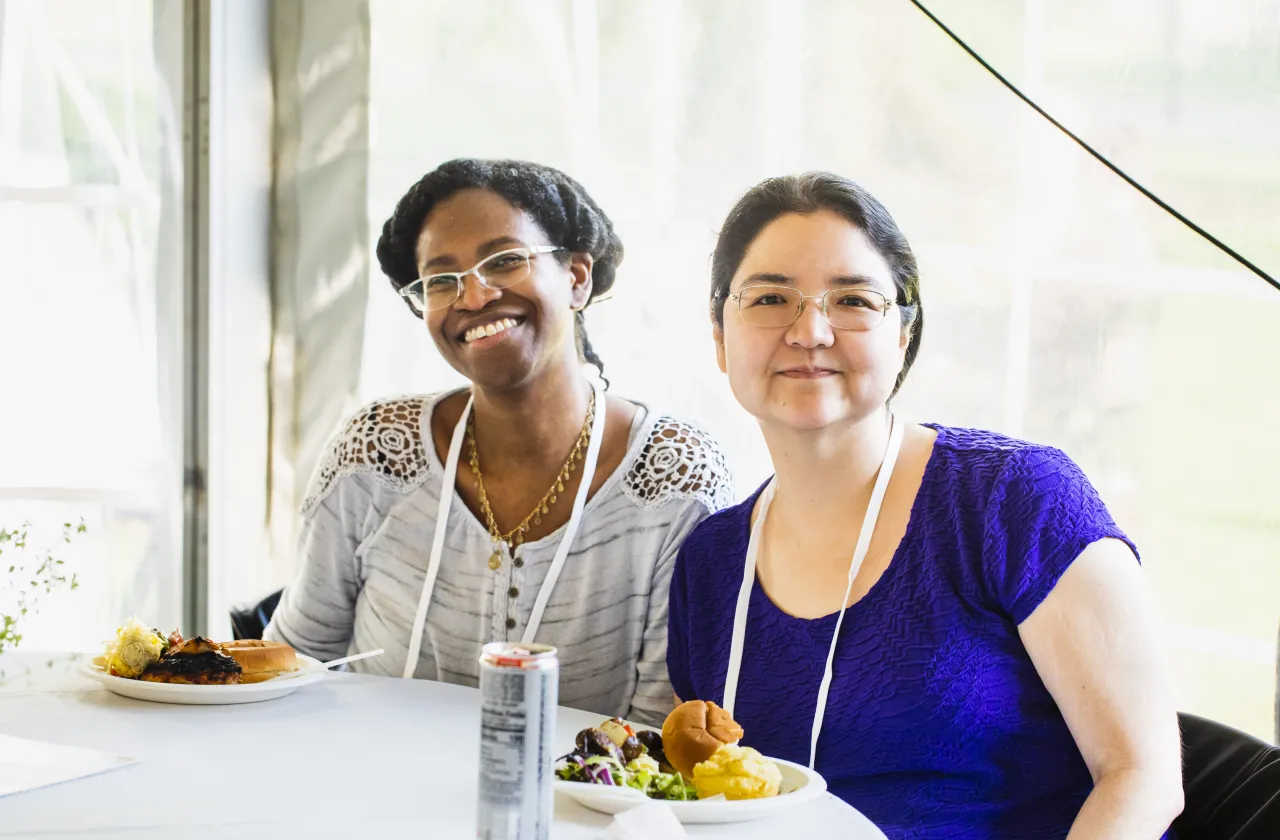 Two alums with plates of food in front of them, smiling at the camera