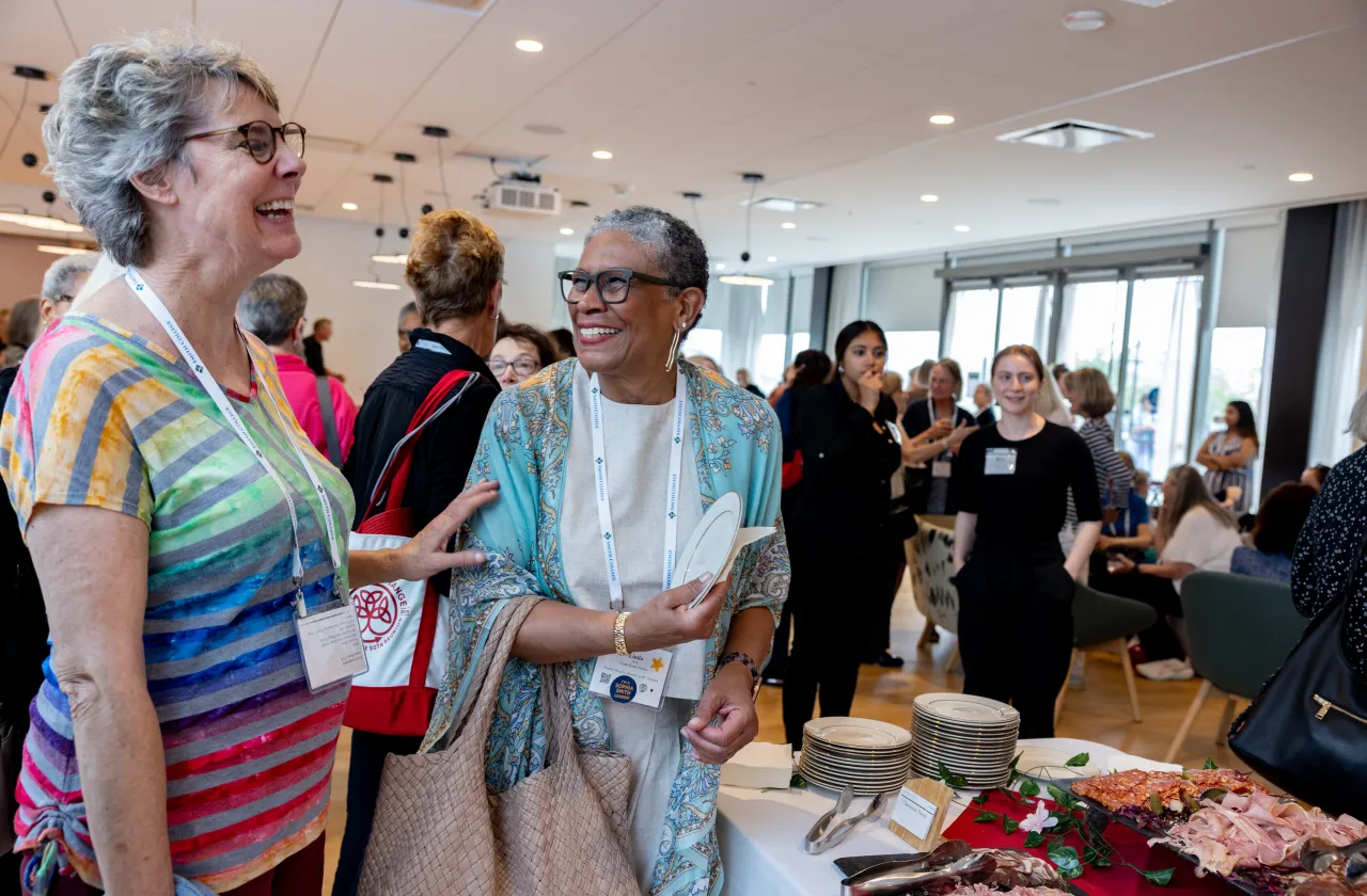 Two alums smiling and looking at each other while picking up plates, preparing to eat