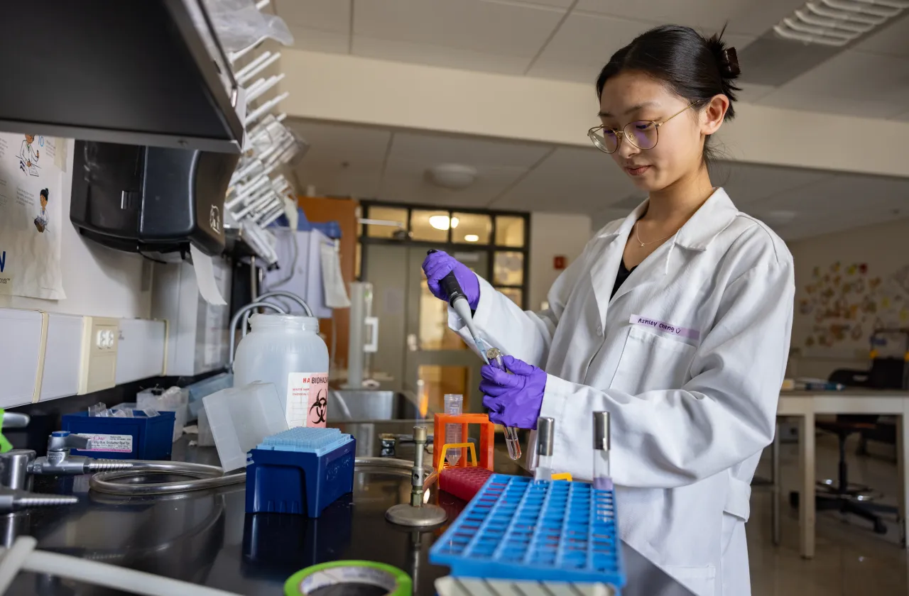 A student in a white lab coat holds a pipette