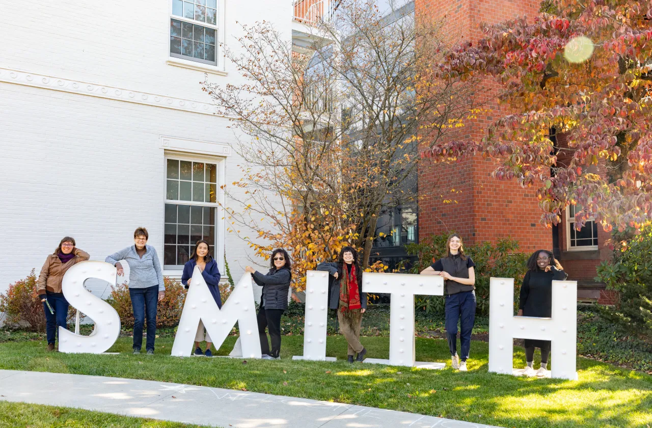 Alums standing next to large letters that spell "SMITH" in front of the Alumnae House