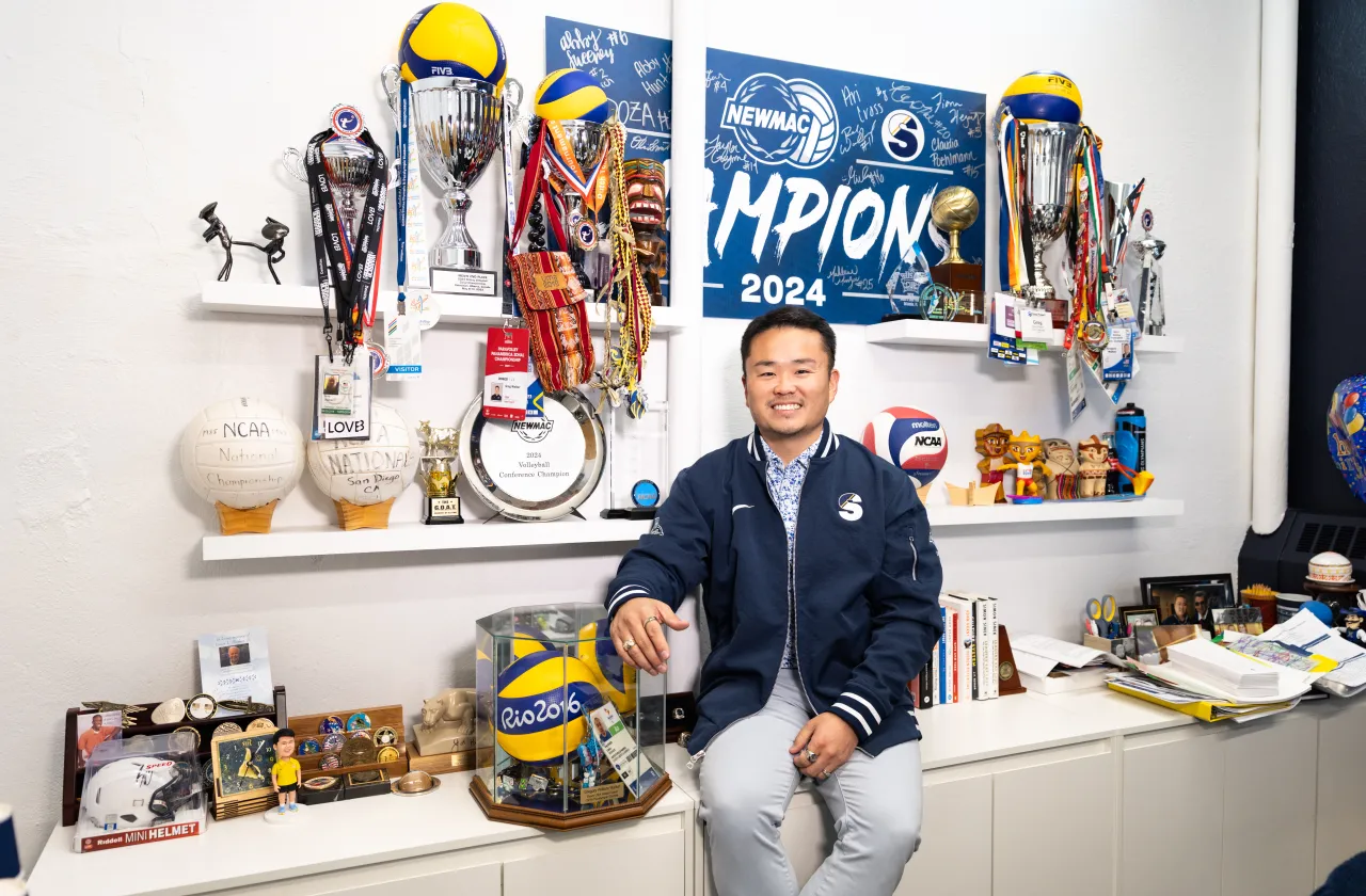 Greg Walker smiles in front of a wall of awards in his office.