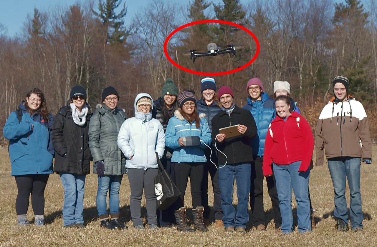 Group of students facing camera with drone hovering above