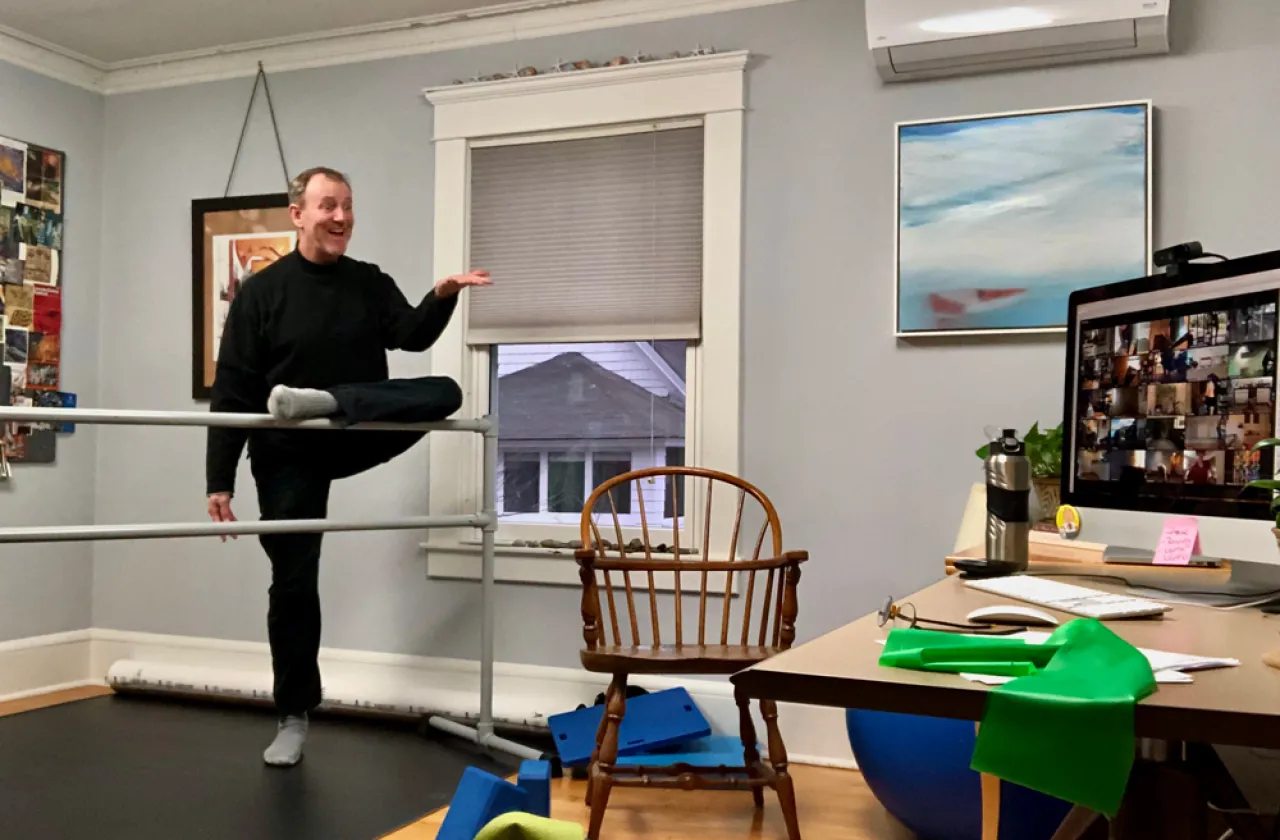 Rodger Blum at a ballet barre with a zoom array of photos on a computer in front of him.