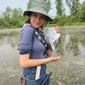 Sophia Holmes in a pond holding up a specimen bag