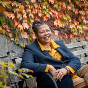 Sarah Willie-LeBreton smiling outdoors and sitting on a bench.