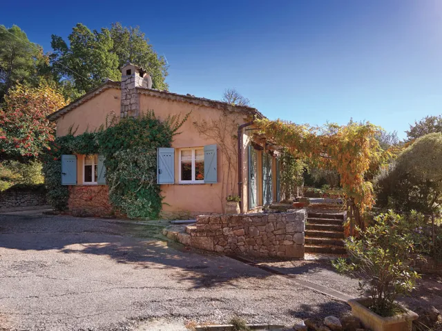 Small terra-cotta cabin with ivy, a lush garden, and a bright blue sky