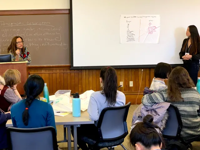 Monica Dean at a podium while a student presents a hand-drawn poster to a class