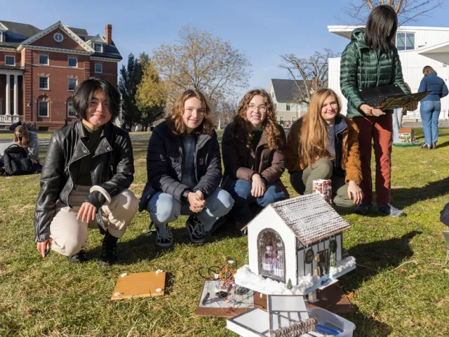 Students kneeling by their cottage like tiny house