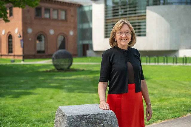 President McCartney smiling outside in a red and black dress, posed in front of Neilson Library in the distance