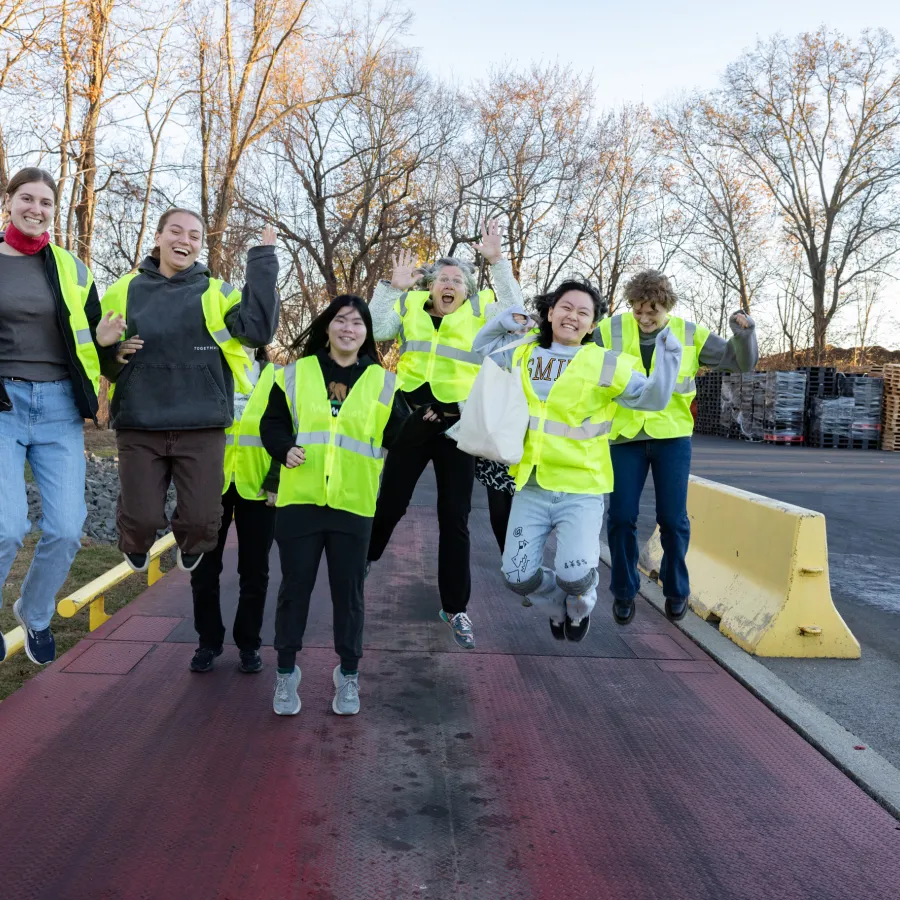 A group of Smith students in bright yellow vests jump on a scale at Vanguard Renewables