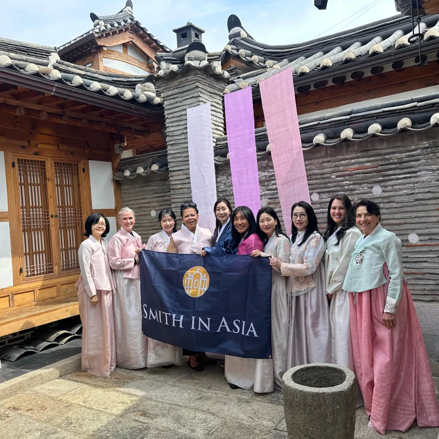 Ten women, including President Willie-LeBreton and Smith Alums, dressed in traditional Korean clothing hold a Smith in Asia banner while standing in front of an historic building in Seoul South Korea