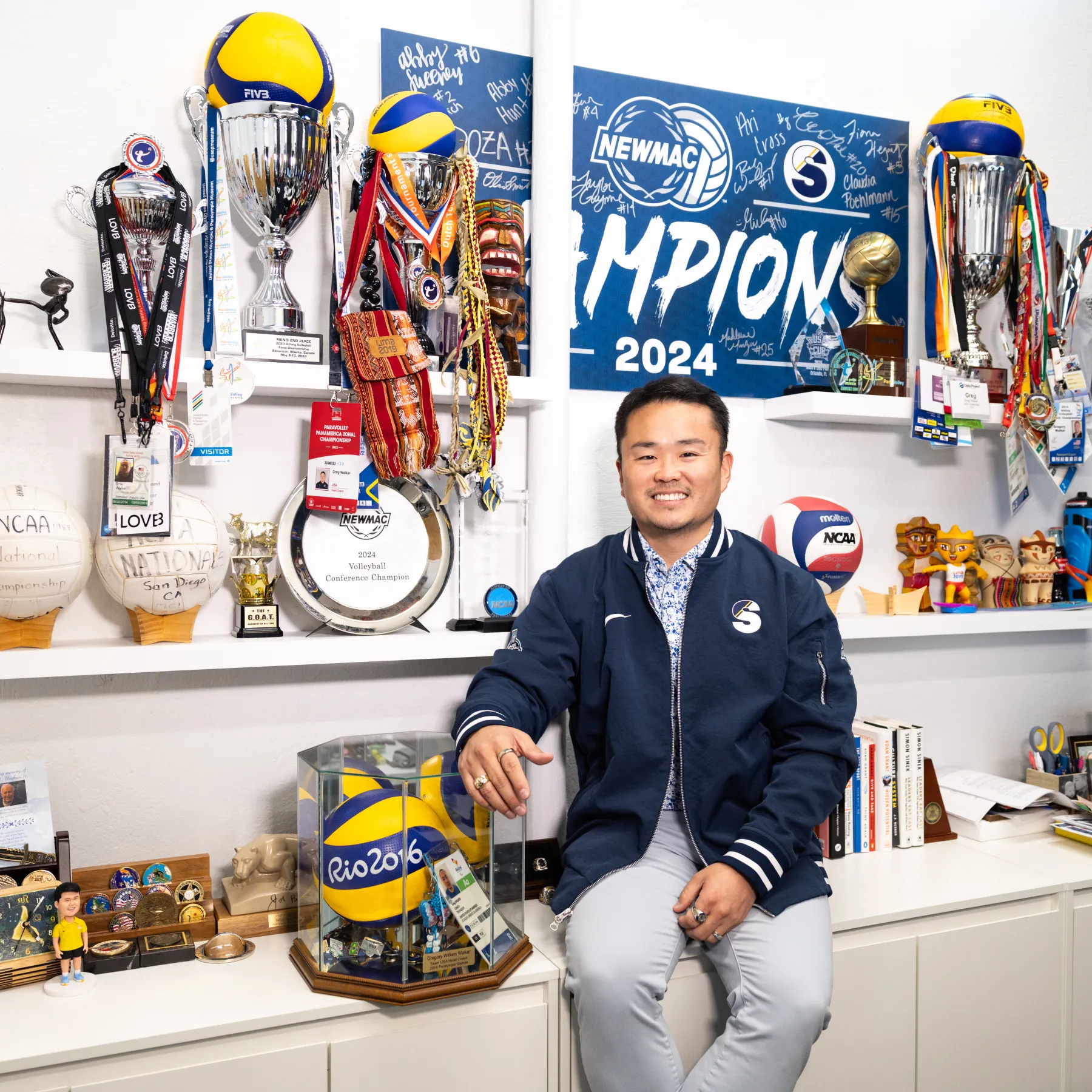 Greg Walker smiles in front of a wall of awards in his office.