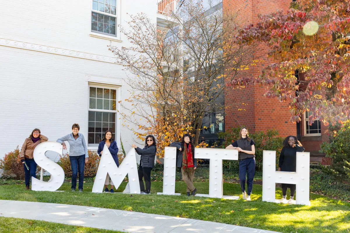 Alums standing next to large letters that spell "SMITH" in front of the Alumnae House