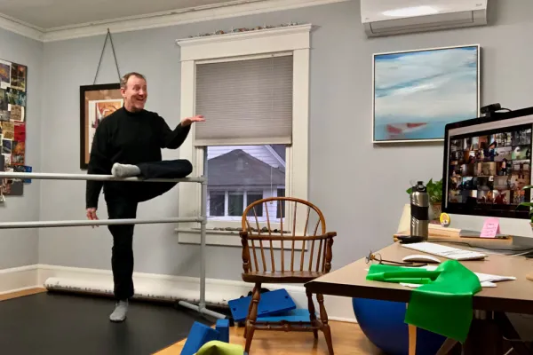 Rodger Blum at a ballet barre with a zoom array of photos on a computer in front of him.