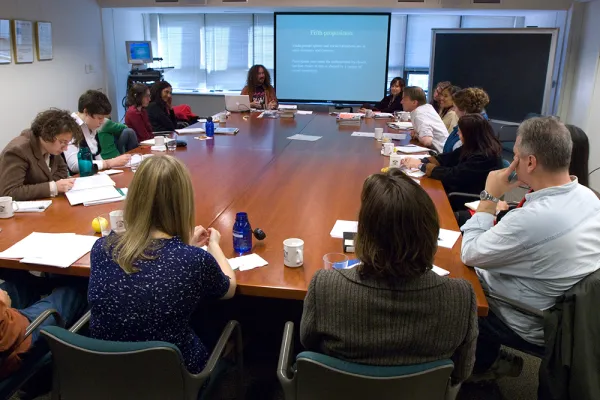 A group of 16 faculty and students meeting around a large table