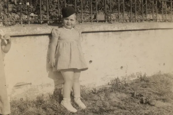 From the college archives: girl (Virginia Apuzzo) in soldier's hat leaning against a garden wall.