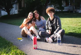 Three students sit on the ground with water bottles.