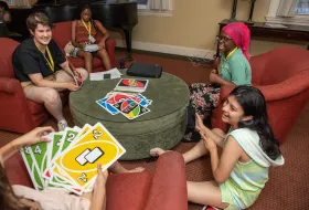 Students sitting in a house living room playing Uno.