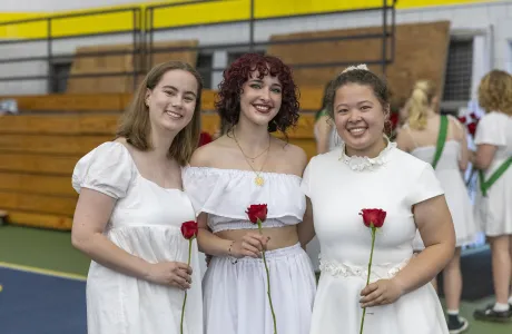 A group of three seniors all dressed in white hold roses and smile on Ivy Day