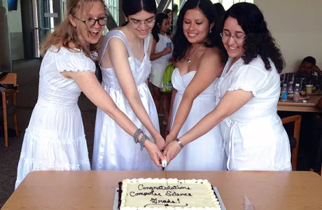 Four computer science grads in Commencement dresses cutting a cake