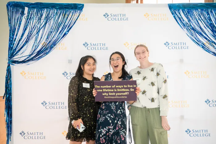 Three students holding up a sign that says "The number of ways to live in one lifetime is limitless. So why limit yourself?" at the senior soiree