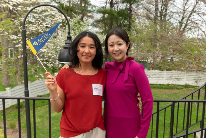 Two students smile at the camera while one waves a Smith pennant