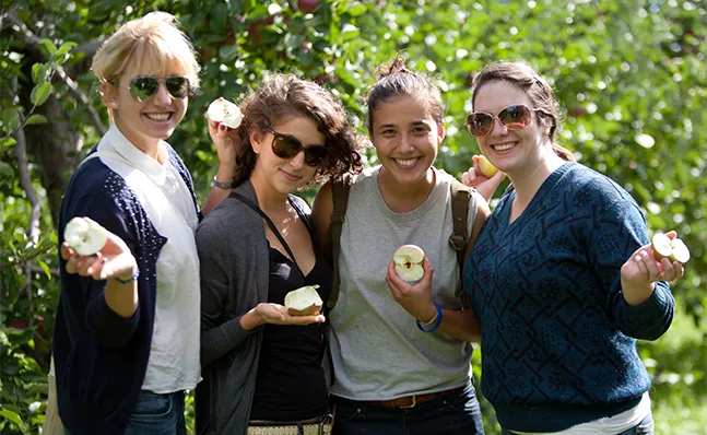 Four students holding half-eaten apples and smiling.