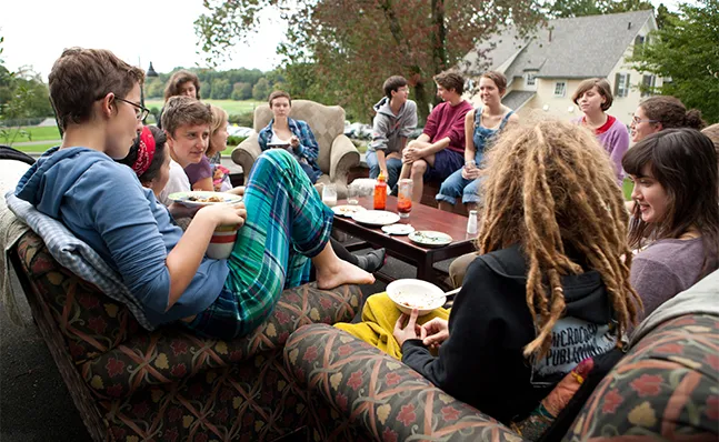 A group of students sitting outside in armchairs, eating breakfast and talking, surrounded by a scenic view.