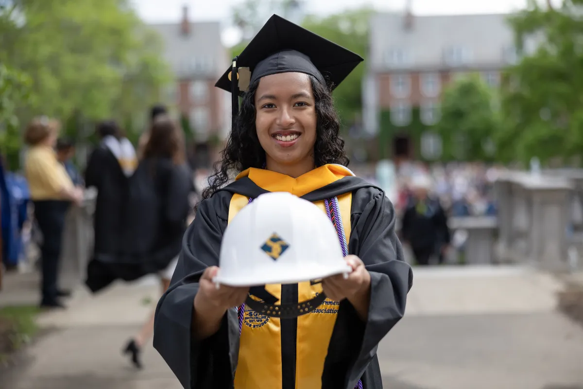 An engineering graduate holds out her Smith hard hat to the camera on Commencement Day