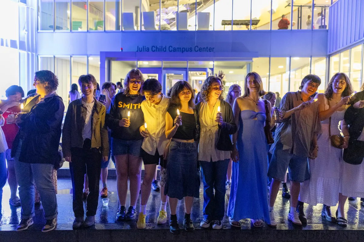 A group of seniors hold candles and laugh on the steps outside the Campus Center during Illuminations