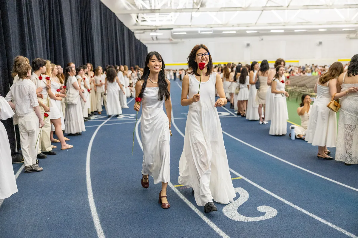 Two seniors hold roses and walk on the indoor track during Ivy Day