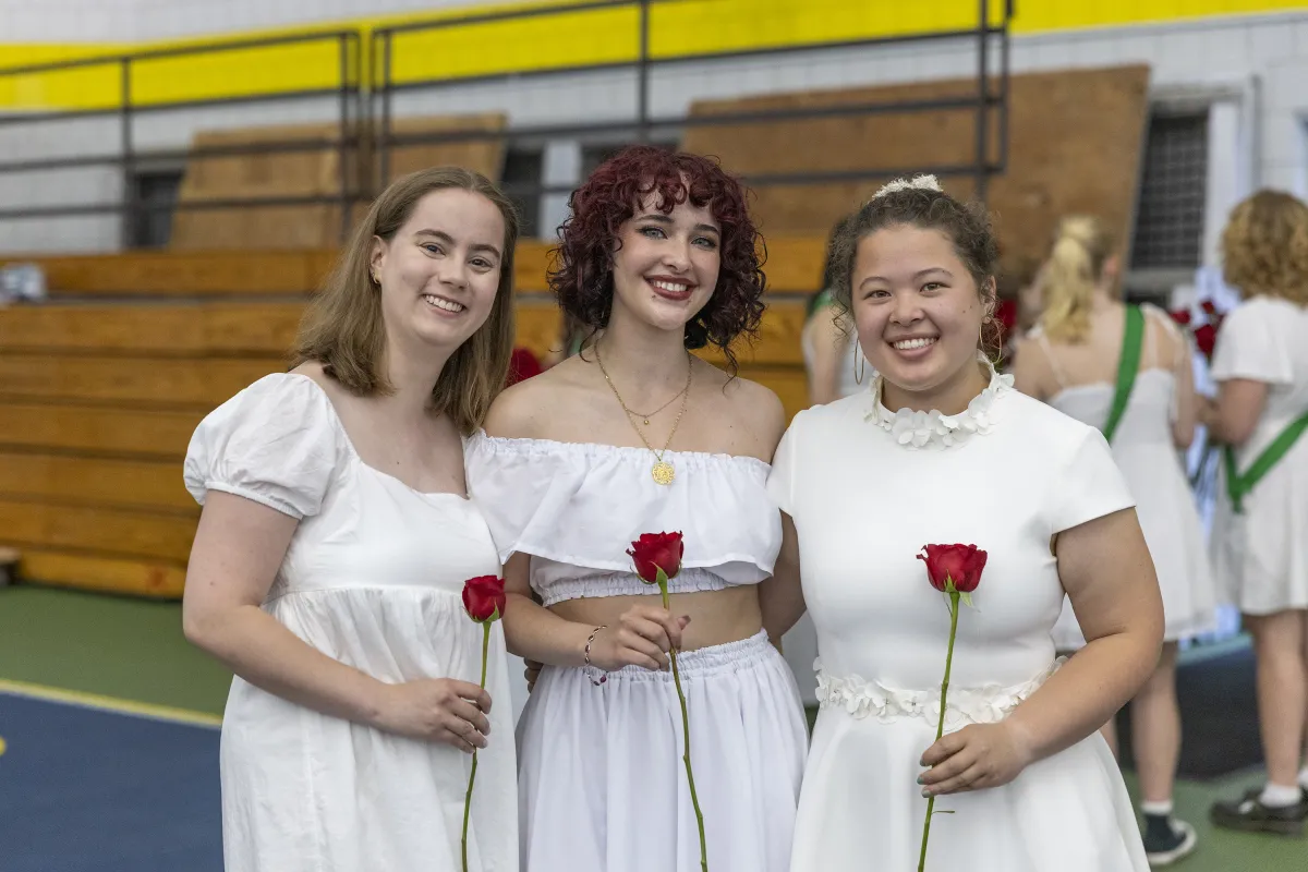 A group of three seniors all dressed in white hold roses and smile on Ivy Day