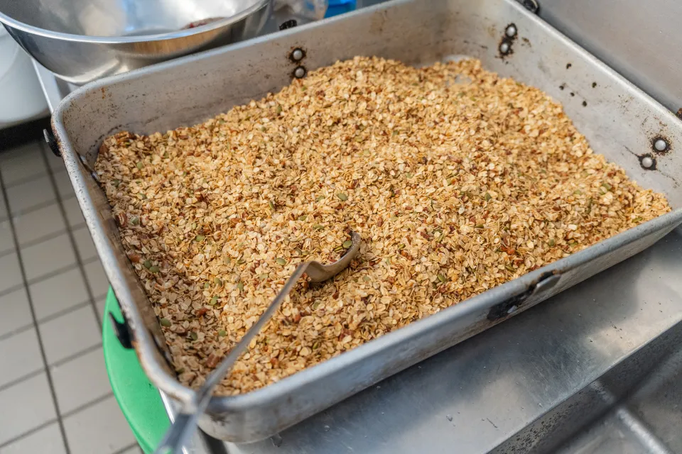 A large silver pan of crunchy cranberry pecan granola with a spoon