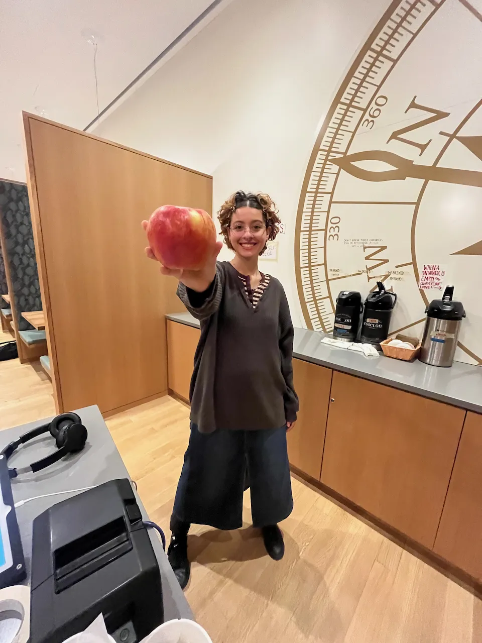 Maya Delmont, smiling, holds out an apple at the Compass Cafe