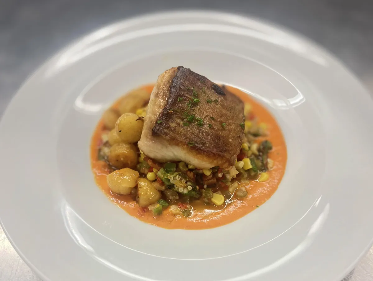 Seared catfish on top of vegetables on a white plate.