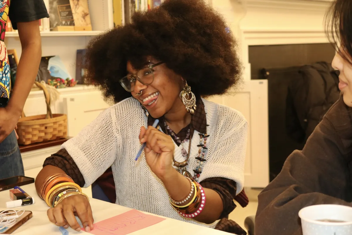 A student holding a pen and paper and smiling at the camera