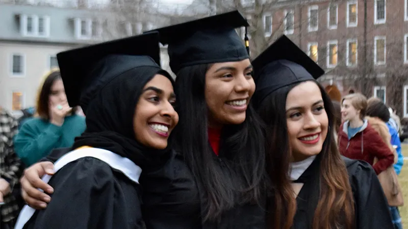 Three students smiling wearing graduation caps and gowns at a student-led March 2020 graduation ceremony